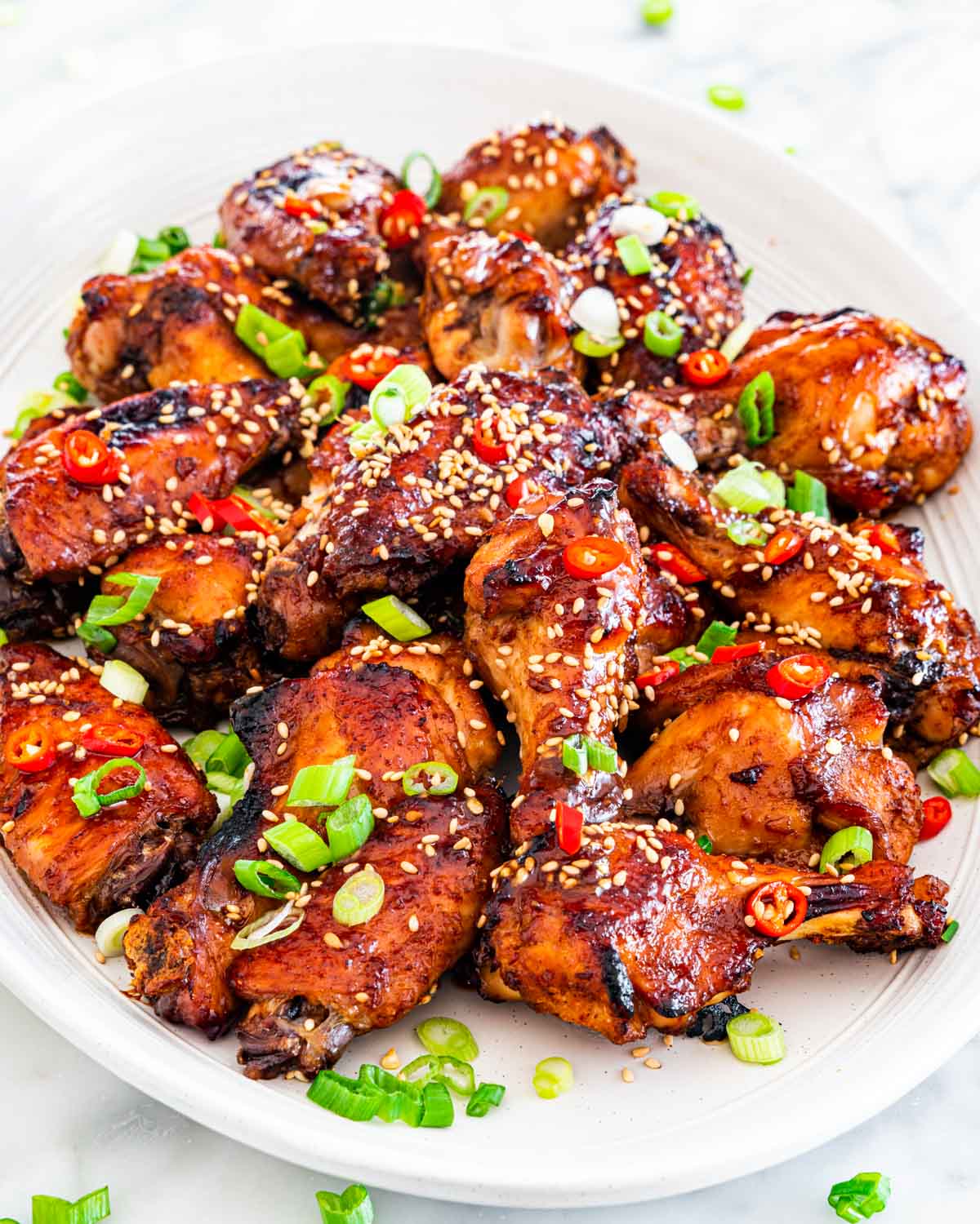 chinese chicken wings on a white platter garnished with green onions, sesame seeds and red chili peppers