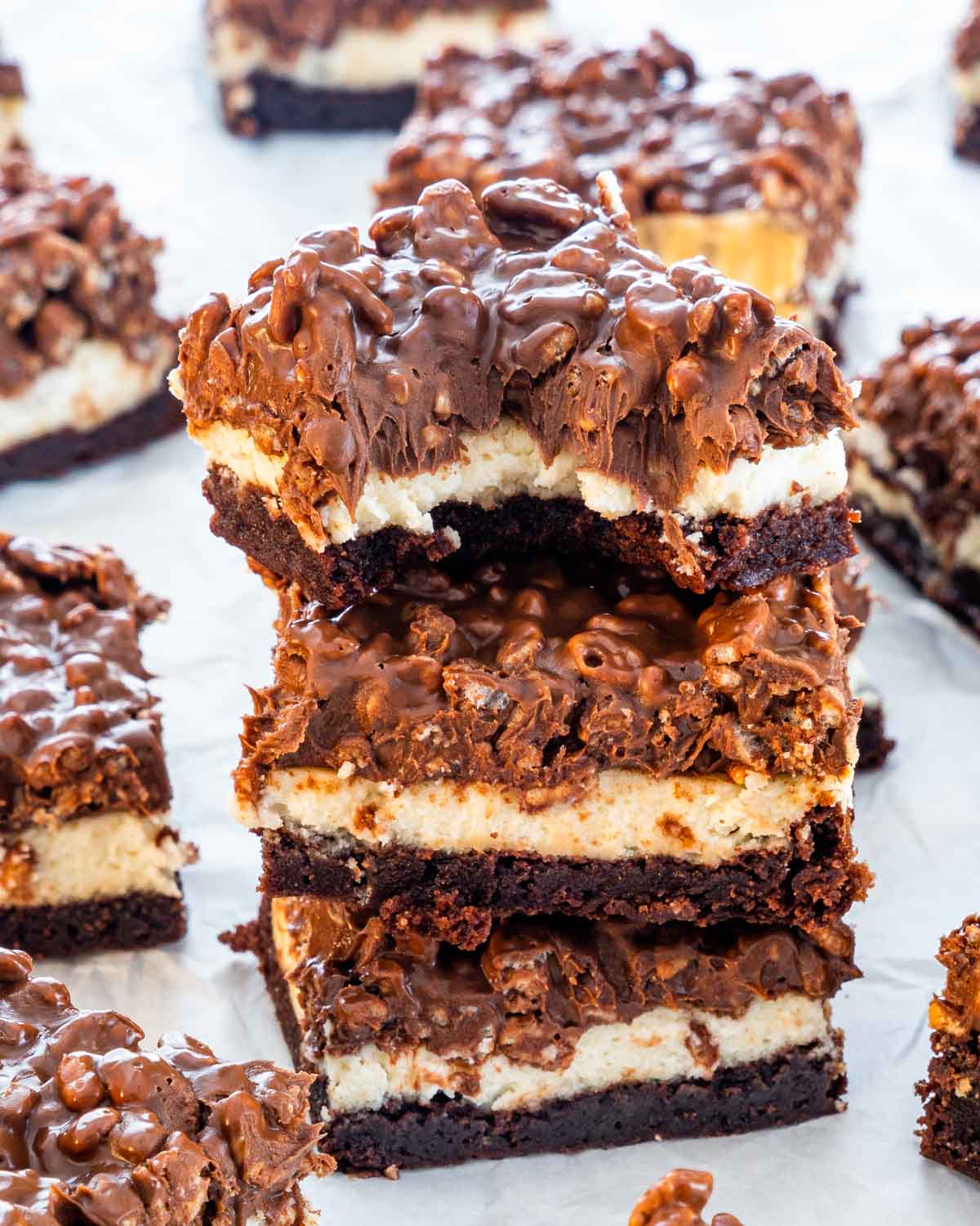 a stack of triple layer rice krispie brownies stacked up with the first one having a bite taken out of it