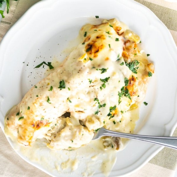 overhead shot of white chicken enchiladas on a plate with a fork taking a bite