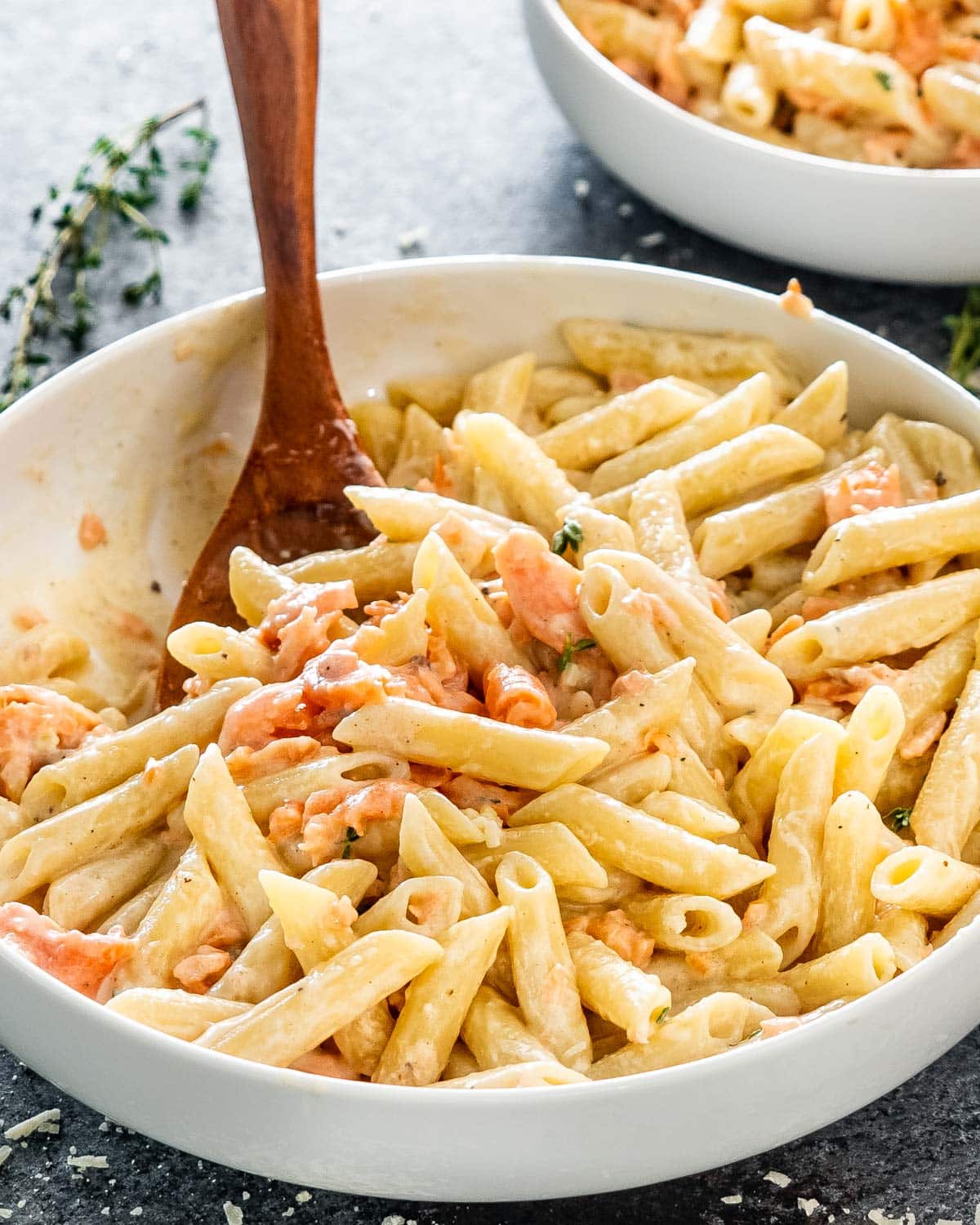 alfredo salmon pasta in a white bowl with a wooden spoon inside.
