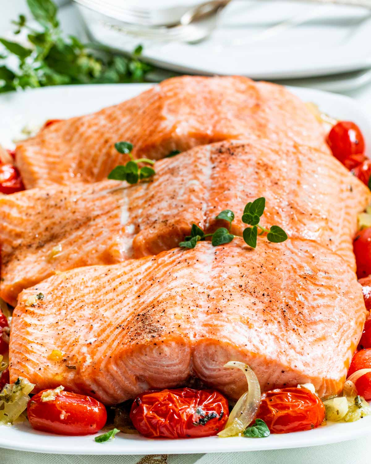 baked salmon with roasted tomatoes on a white serving platter.