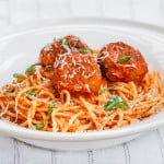 a bowl full of spaghetti topped with three chicken meatballs