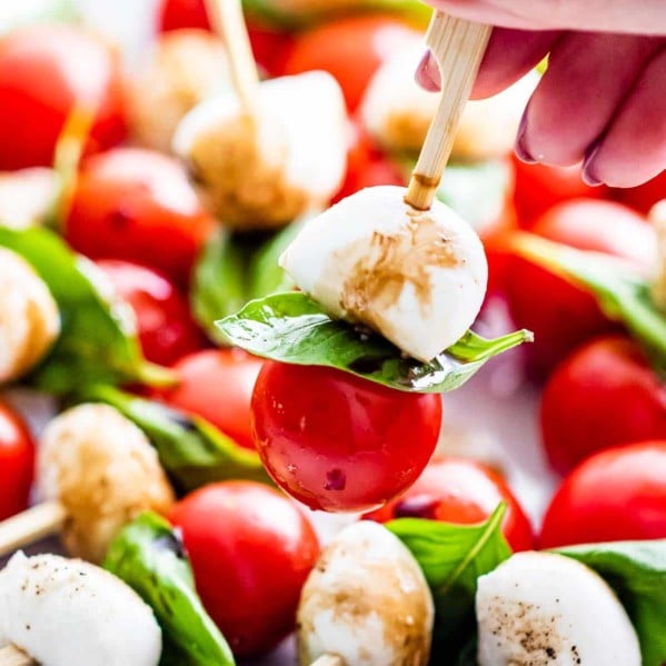 and hand holding a caprese salad bite on a pick over a plate full of them