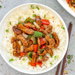 a serving of szechuan pork on a bed of jasmine rice in a white bowl.