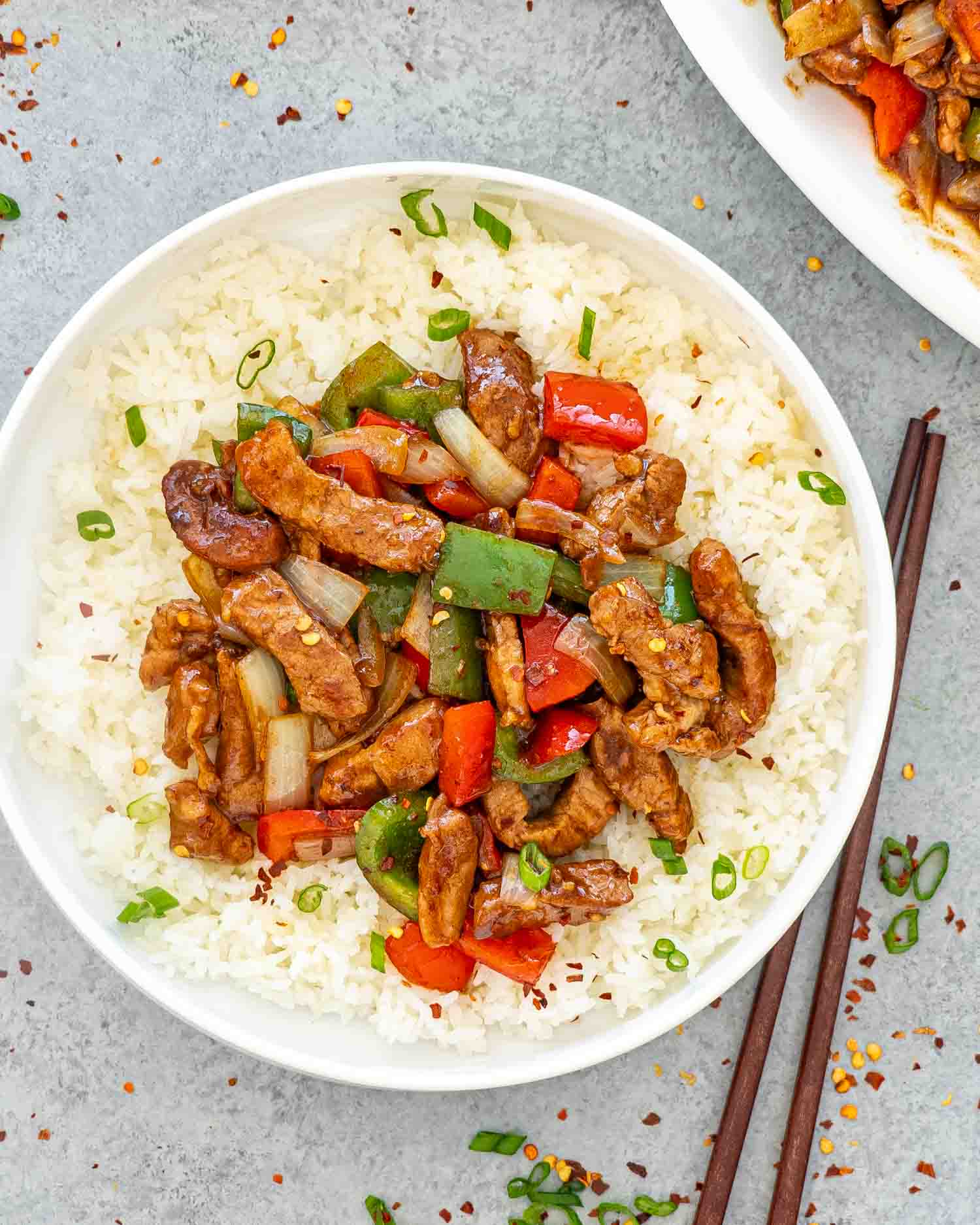 a serving of szechuan pork on a bed of jasmine rice in a white bowl.