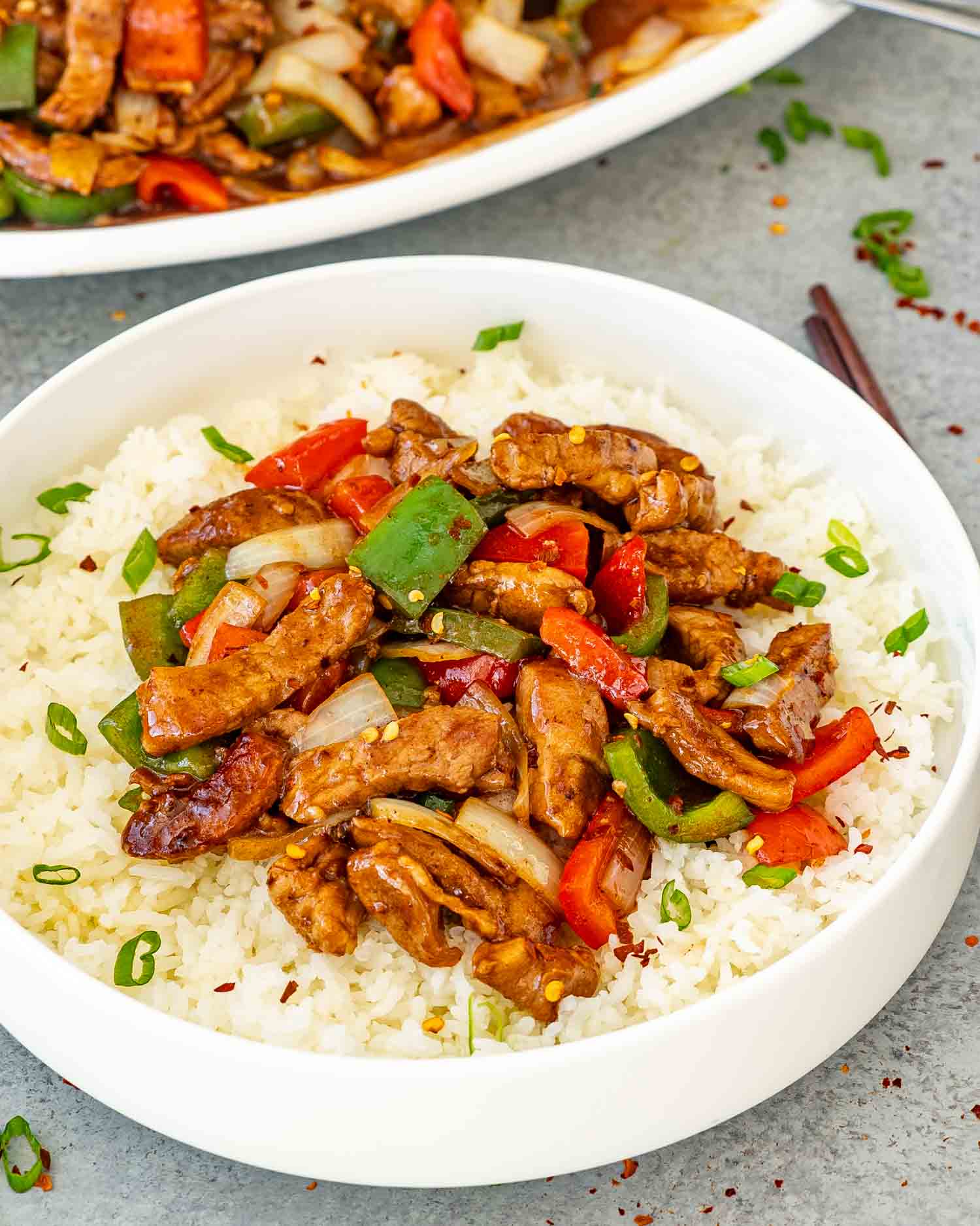 a serving of szechuan pork on a bed of jasmine rice in a white bowl.