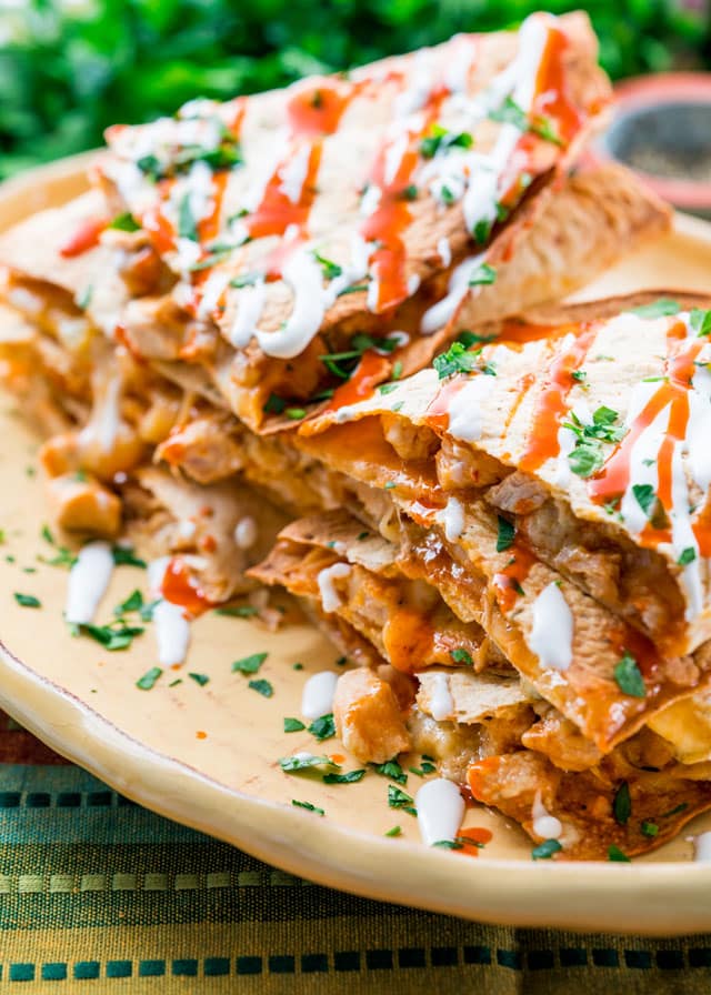a platter piled with chicken quesadillas topped with sour cream, hot sauce, and parsley