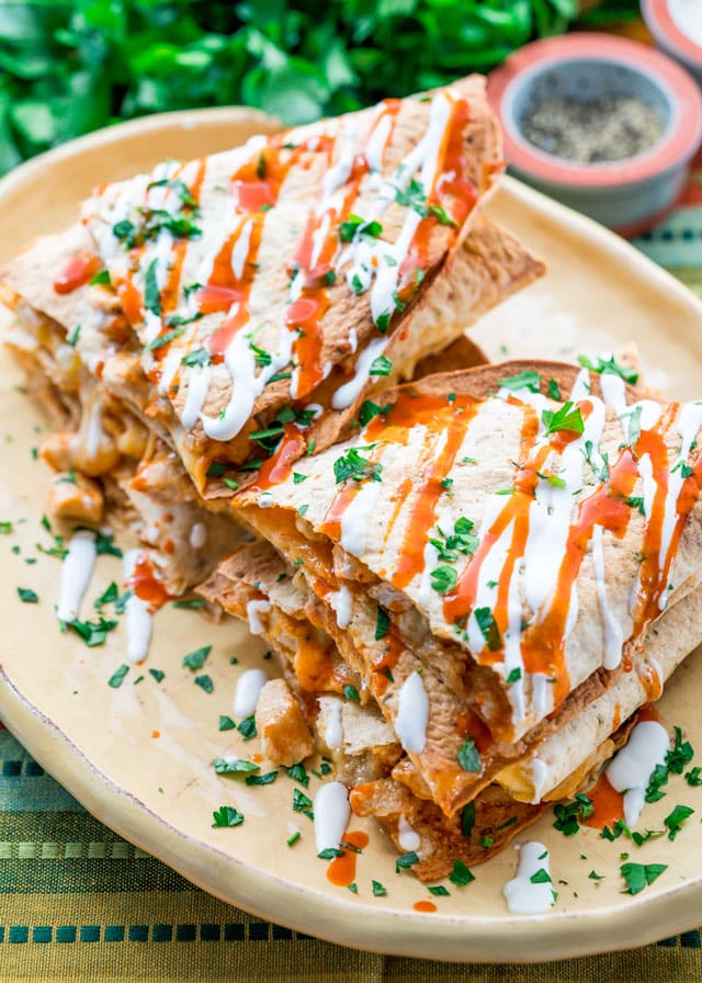 a platter piled with chicken quesadillas topped with sour cream, hot sauce, and parsley