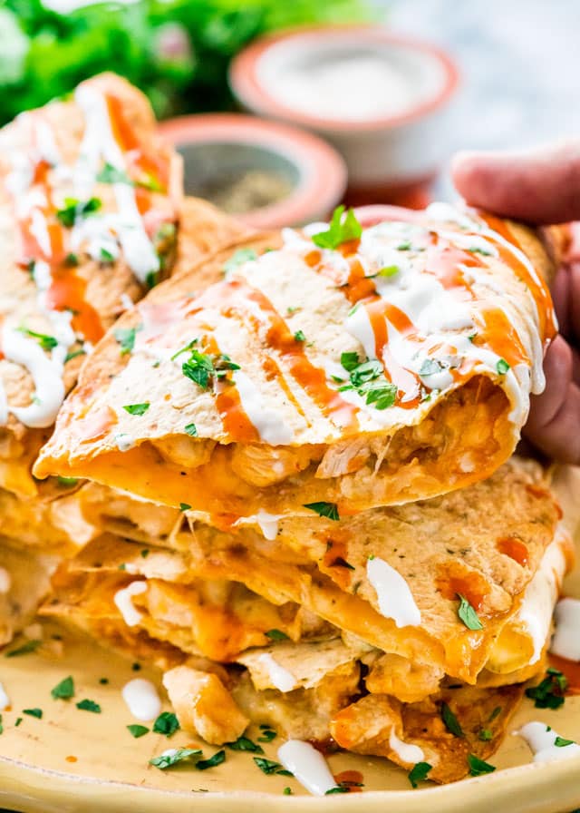 holding a chicken quesadilla with sour cream, hot sauce, and parsely
