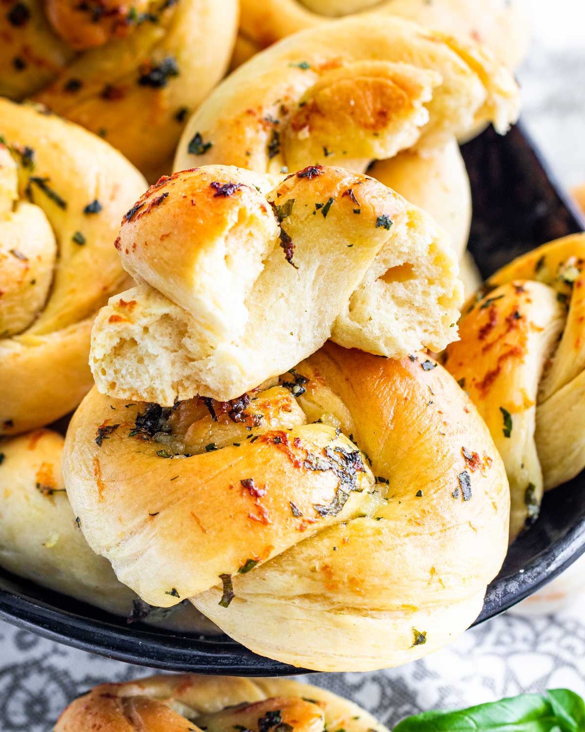 side view shot of garlic knots in a bread bowl with the top one broken in half and with some garlic knots surrounding the bowl