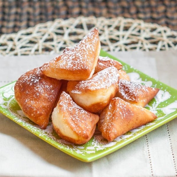 a plate of mandazi african donuts dusted with powdered sugar