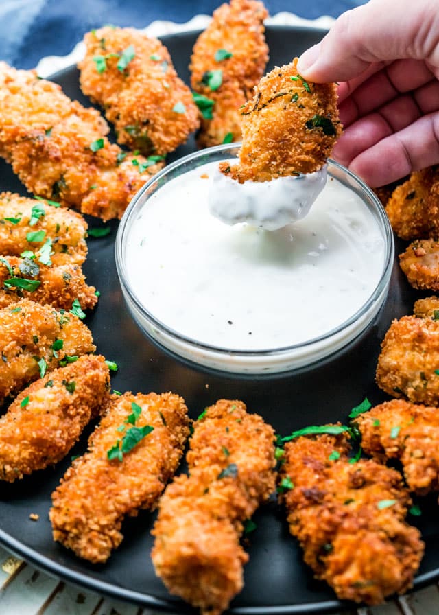 a plate of parmesan chicken strips with a bowl of ranch dressing in the middle