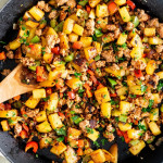 overhead shot of sausage and potato hash being stirred by a wooden spoon