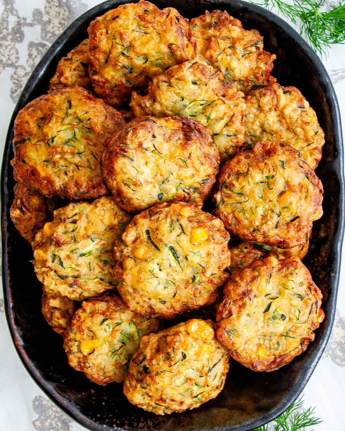 overhead shot of a bunch of zucchini corn fritters on a black platter
