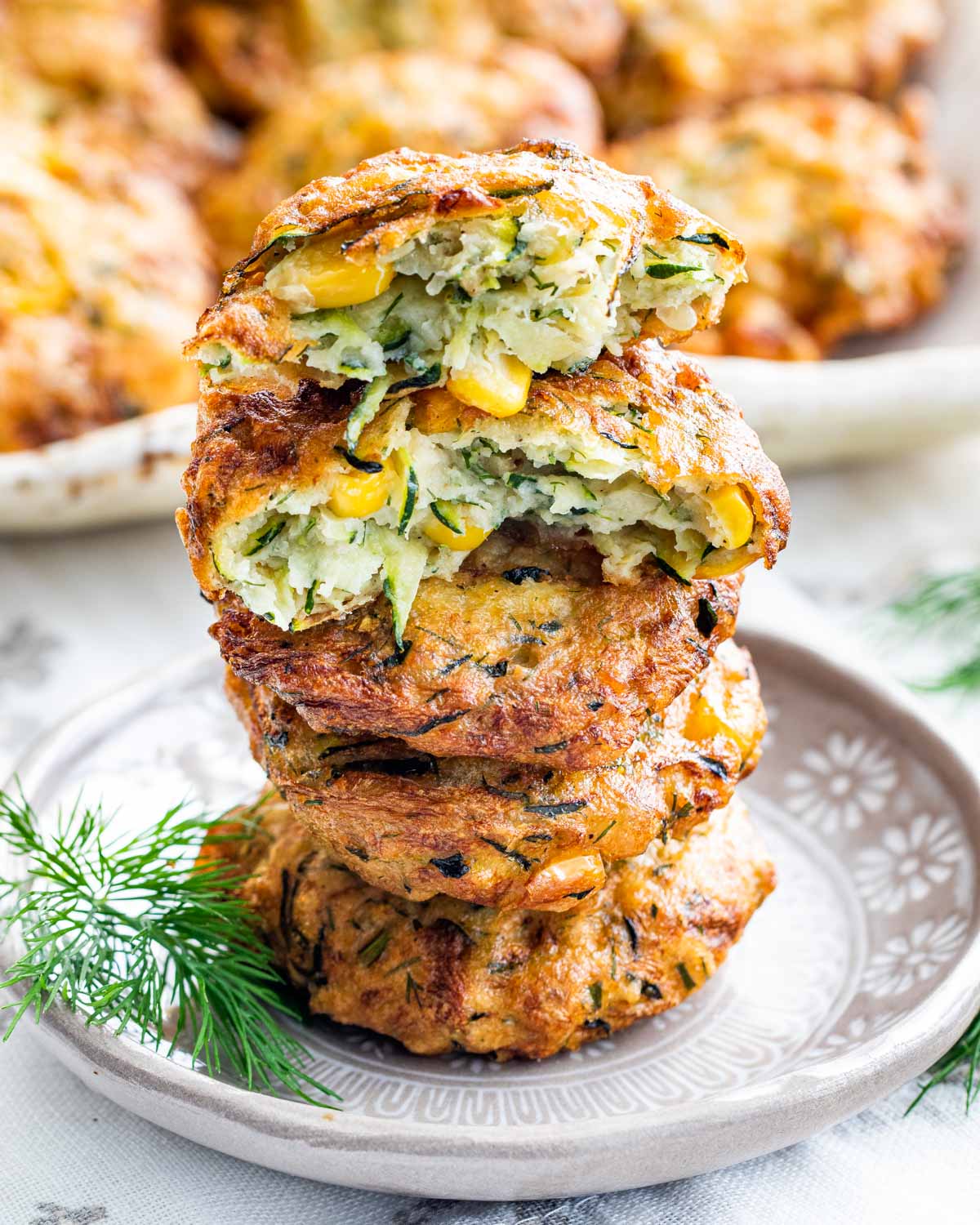 a stack of zucchini corn fritters stacked on top of each other on a plate with the top one broken in half