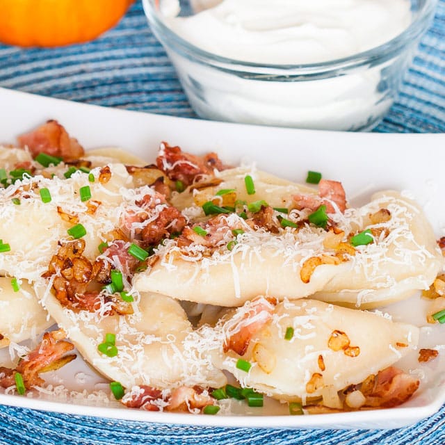 Bacon and Cheese Pirogies on a plate topped with chopped bacon, green onion and grated parm.