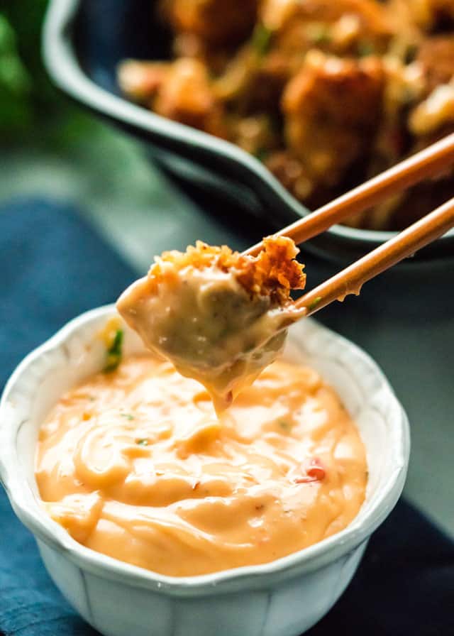 chopsticks holding a piece of crispy chicken after dipping it into a bowl of spicy mayo