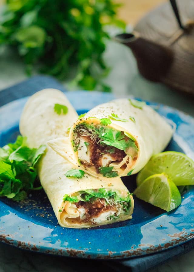 a crispy chicken wrap with micro greens and lime wedges