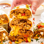 a stack of chicken burritos with a hand holding the top one.