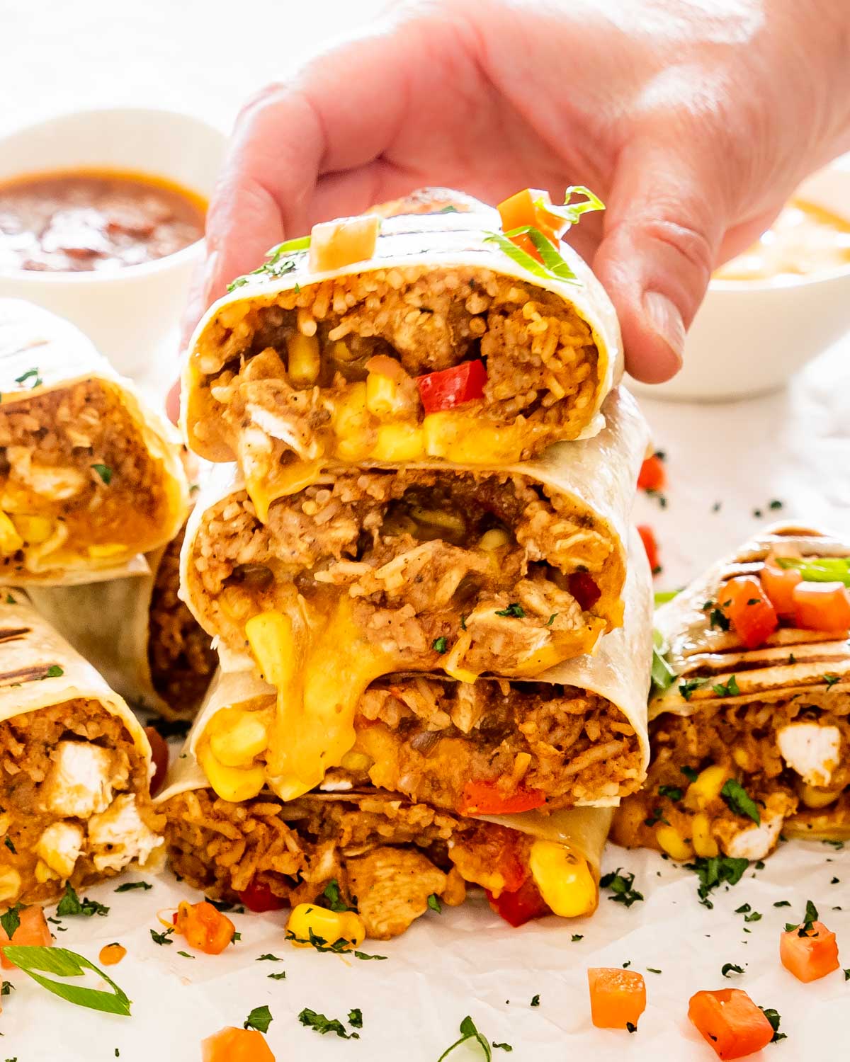 a stack of chicken burritos with a hand holding the top one.