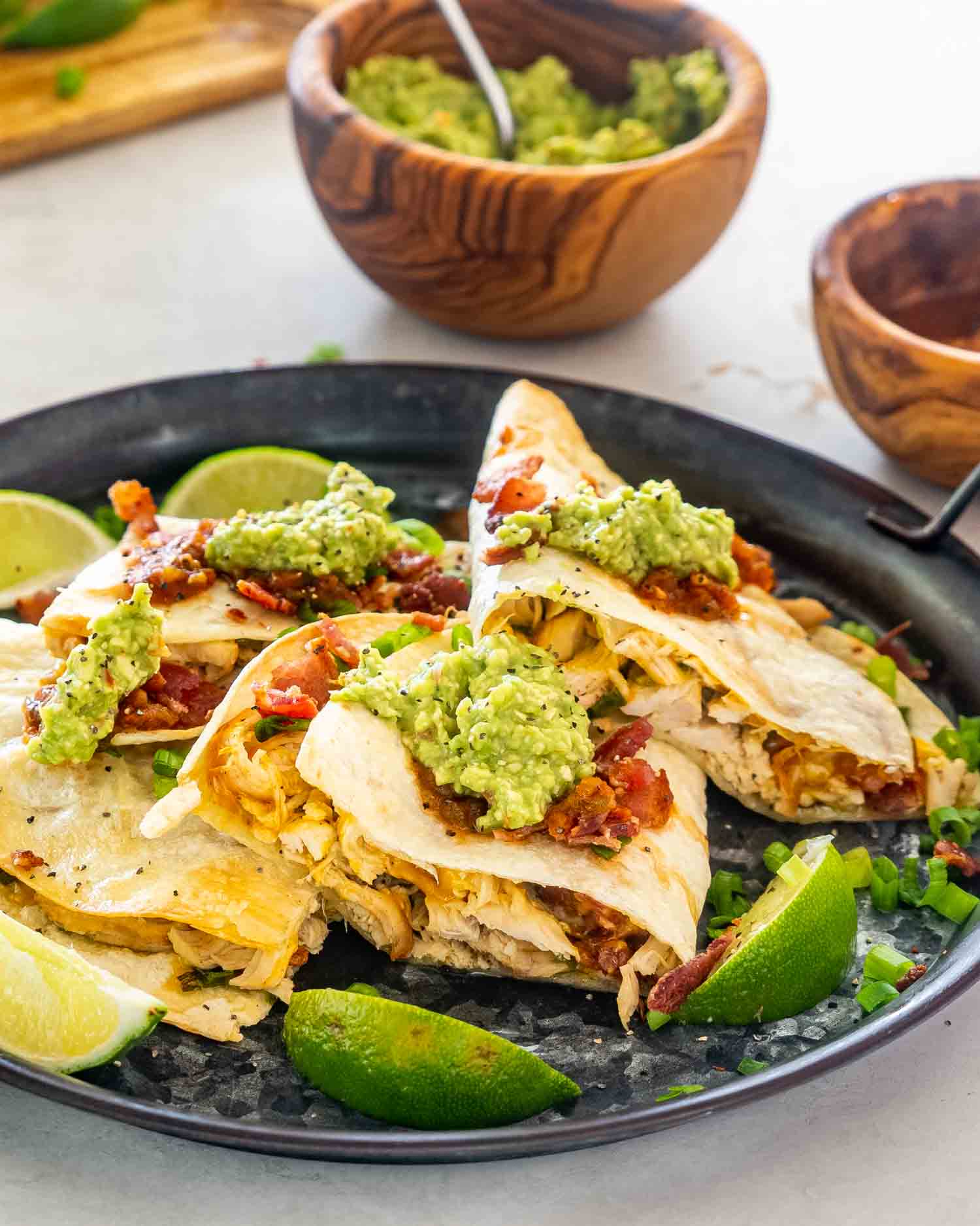 chicken quesadillas on a metal plate topped with avocado and salsa.