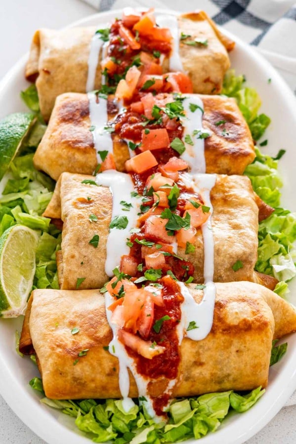 chimichangas on a serving platter on a bed of lettuce garnished with salsa and sour cream.