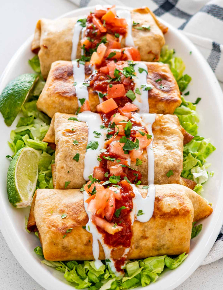 chimichangas on a serving platter on a bed of lettuce garnished with salsa and sour cream.