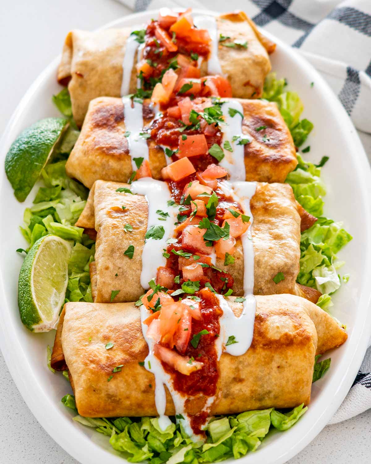 chimichangas on a serving platter on a bed of lettuce garnished with salsa and sour cream.