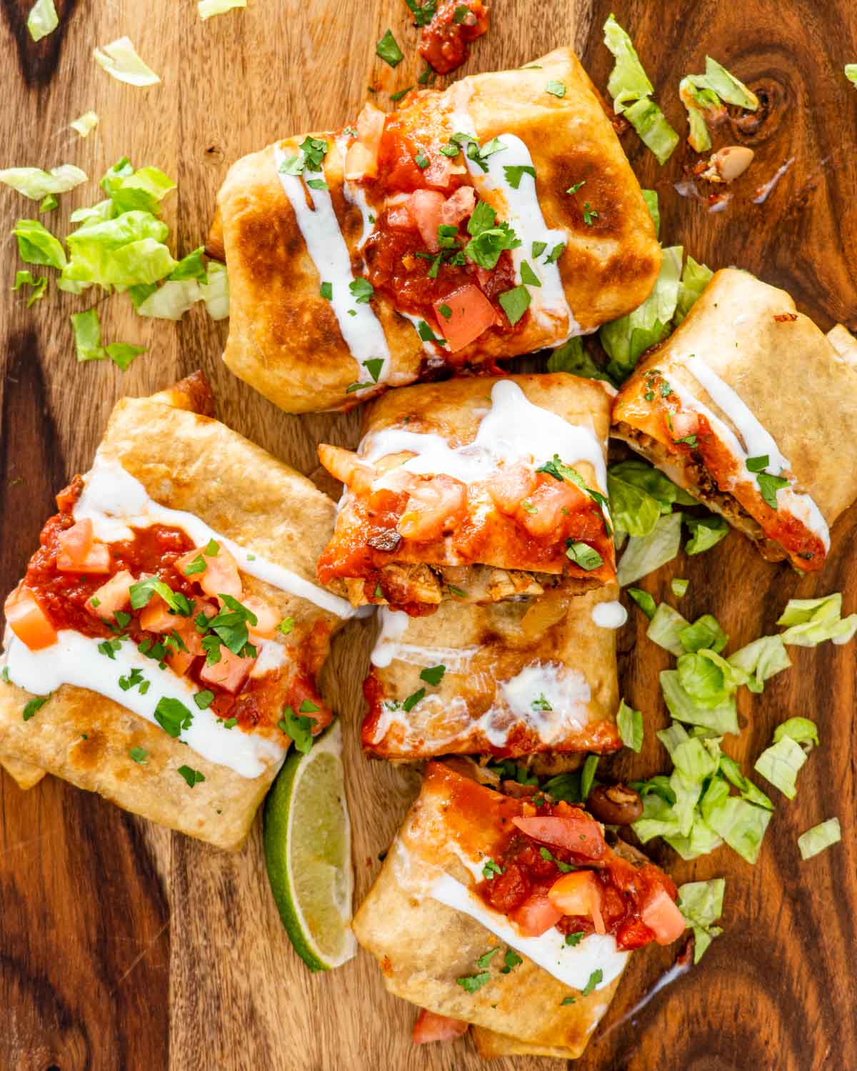 overhead shot of chimichangas on a cutting board garnished with salsa and sour cream.