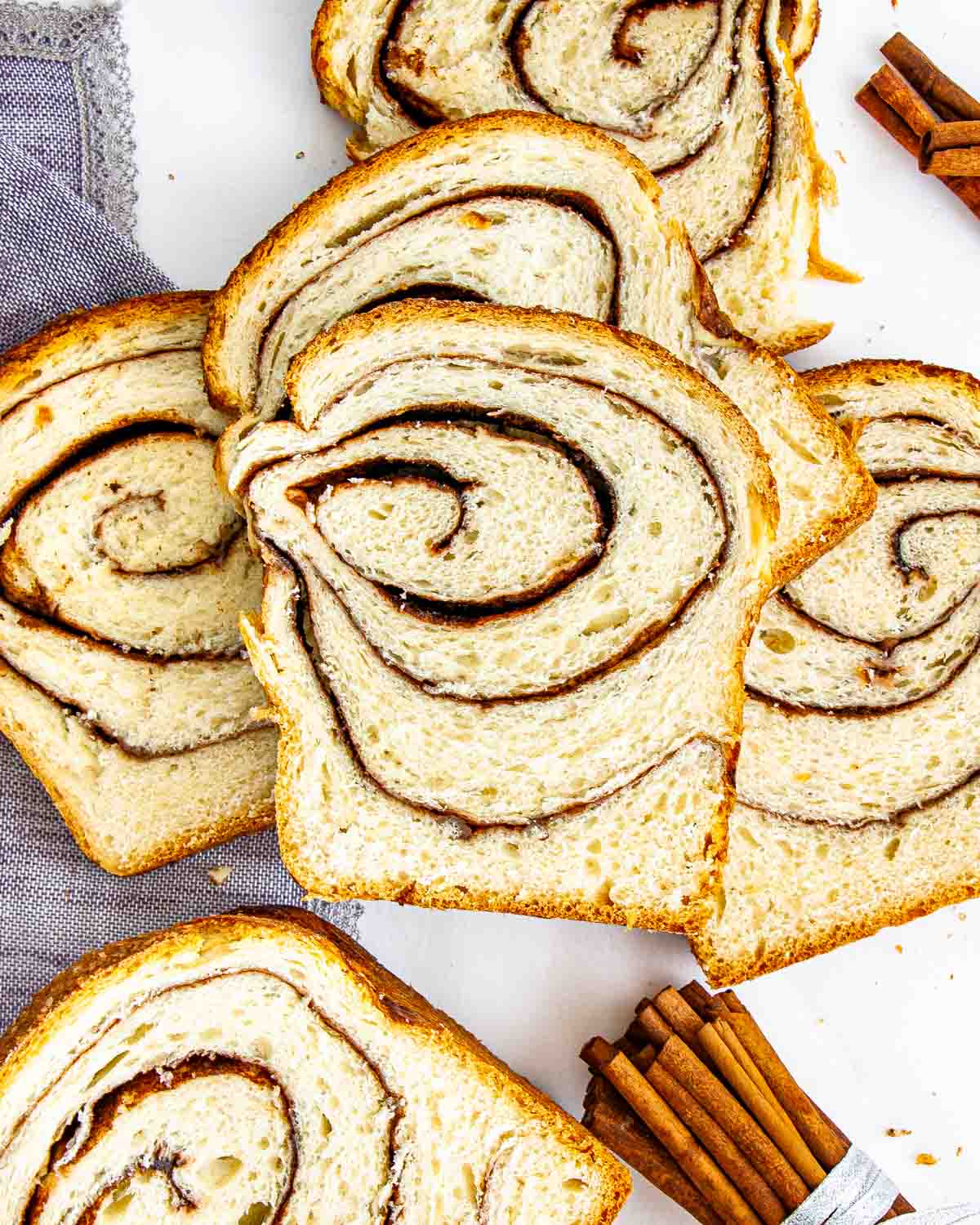 a few slices of freshly baked cinnamon bread next to a couple cinnamon sticks.