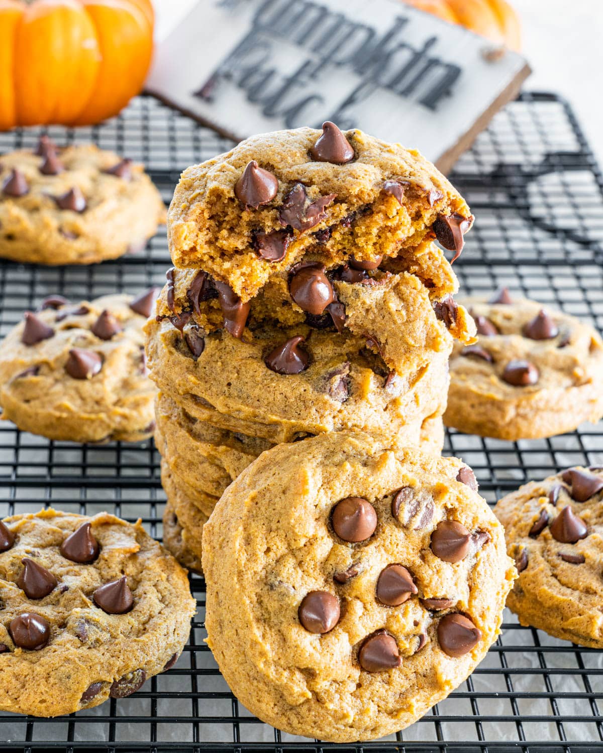 a stack of Pumpkin Chocolate Chip Cookies on a cooling rack with the top cookie broken in half