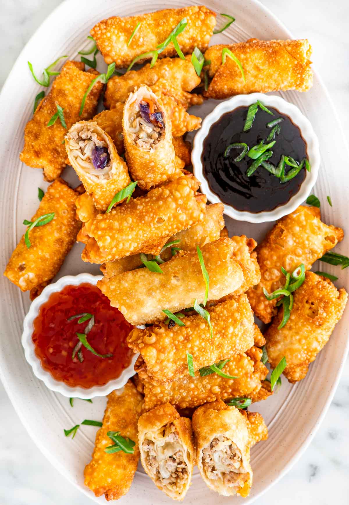 a platter full of freshly made egg rolls with two sauces
