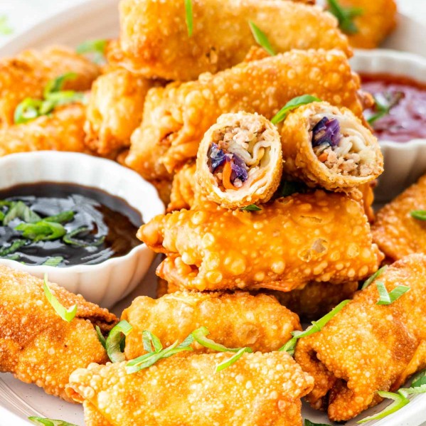 a platter full of freshly made egg rolls with two sauces