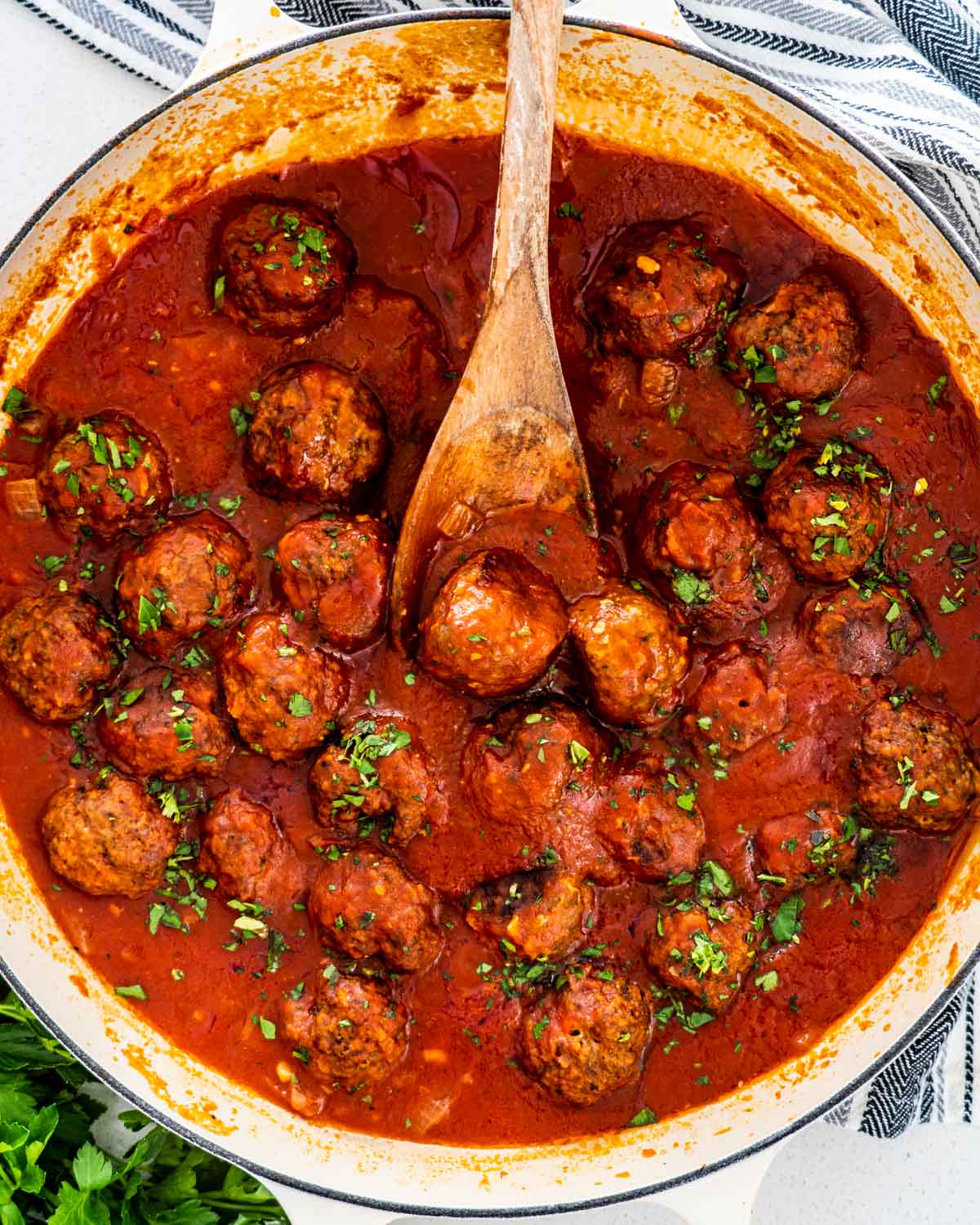 italian meatballs in a dutch oven with a wooden spoon and garnished with parsley.