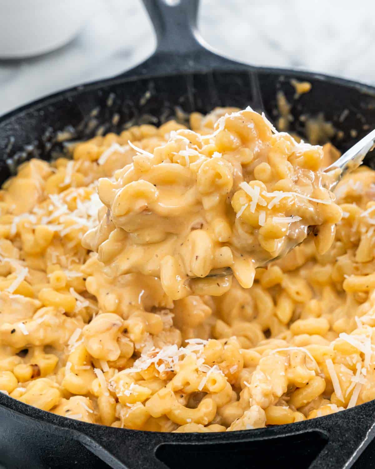 a black skillet with chicken mac and cheese and a spoon picking some up