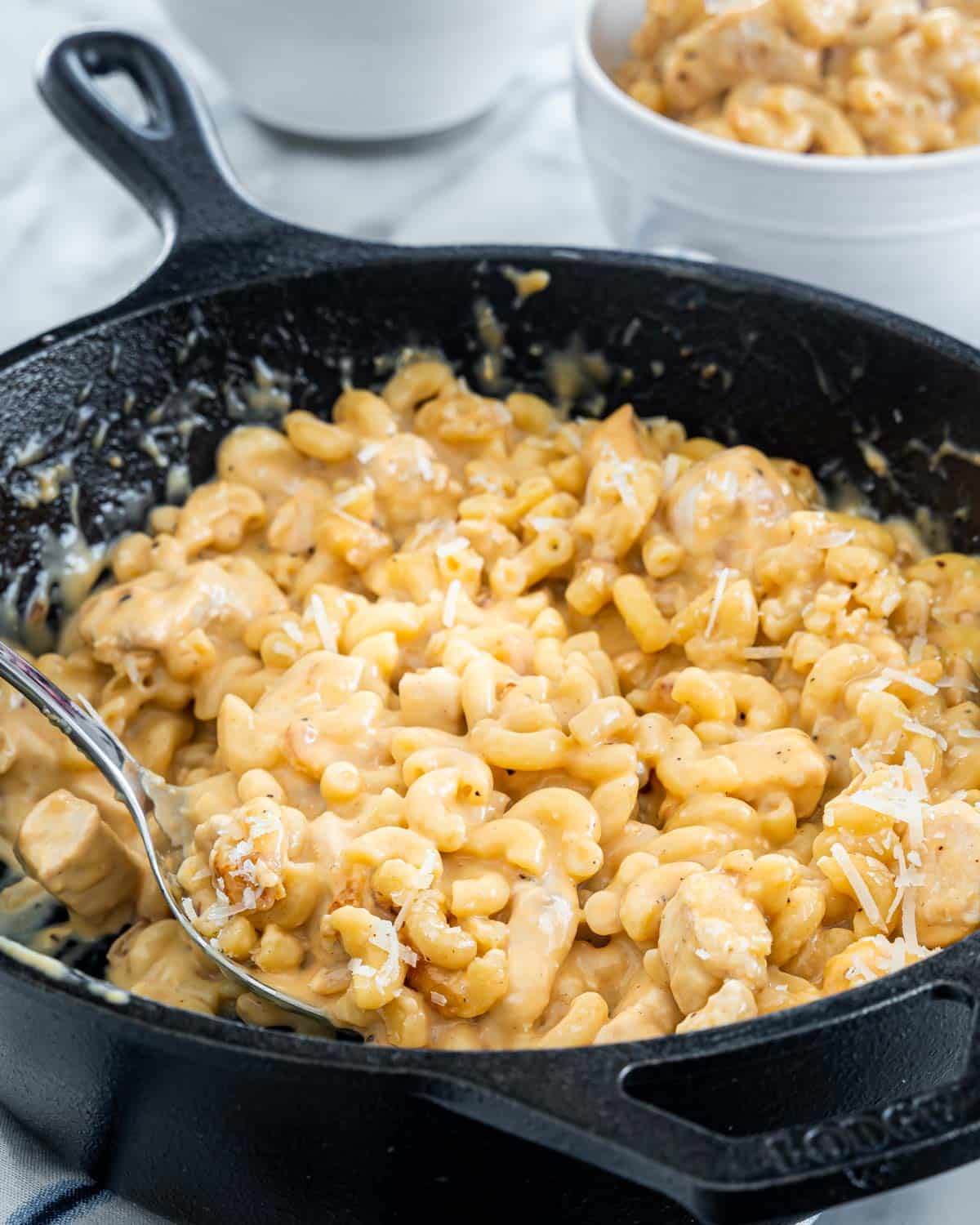a black skillet filled with chicken mac and cheese with a spoon in it