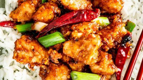 overhead shot of mongolian chicken on top a bed of rice on a plate with chopsticks