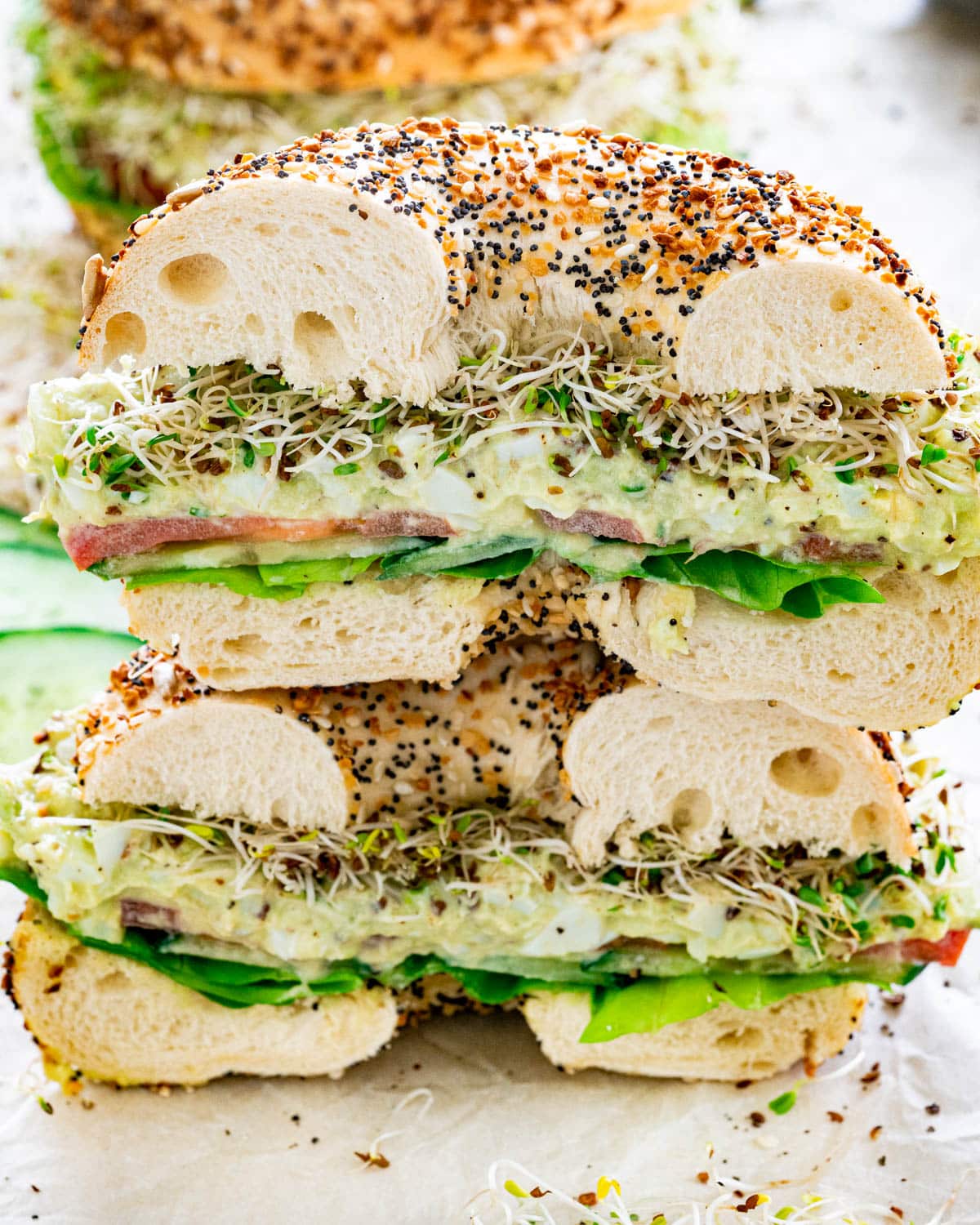 an avocado egg salad bagel cut in half stacked on top of each other