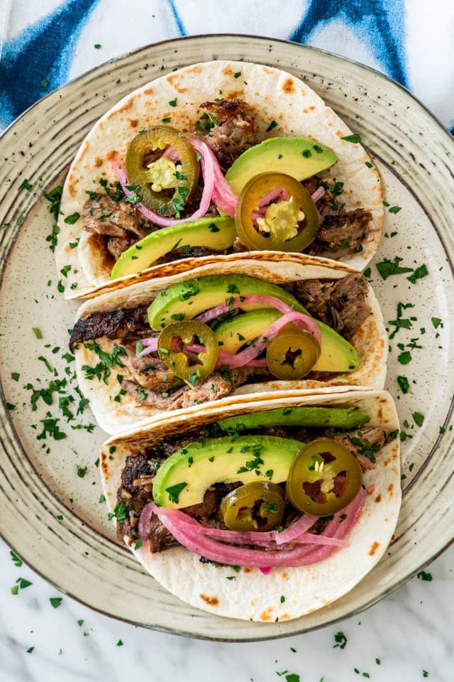 Pork Carnitas tacos topped with avocado, pickled jalapenos and pickled onions