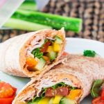 a turkey, hummus and veggie wrap sliced in half on a plate