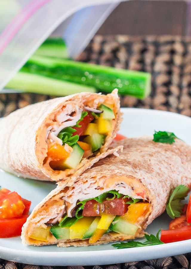 a turkey, hummus and veggie wrap sliced in half on a plate