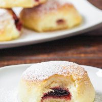 a jam filled baked donut dusted with powdered sugar with a bite taken out of it on a plate