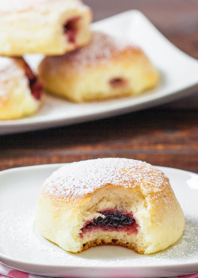 a jam filled baked donut dusted with powdered sugar with a bite taken out of it on a plate