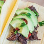 beef carnitas tacos topped with sliced avocado on a plate