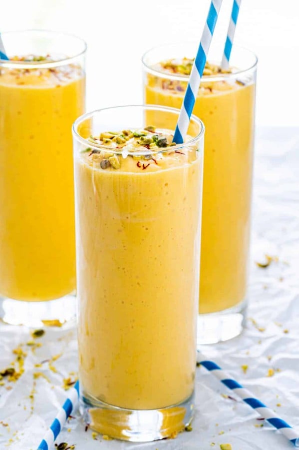side view shot of mango lassis in tall glasses topped with chopped pistachios