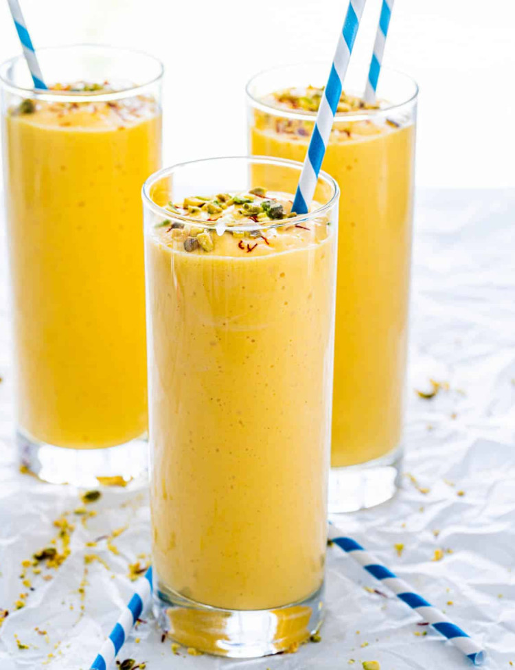side view shot of mango lassis in tall glasses topped with chopped pistachios