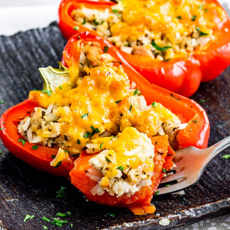 two stuffed pepper halves on a black plate with a fork holding a bite