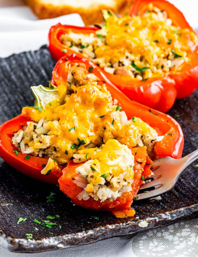two stuffed pepper halves on a black plate with a fork holding a bite