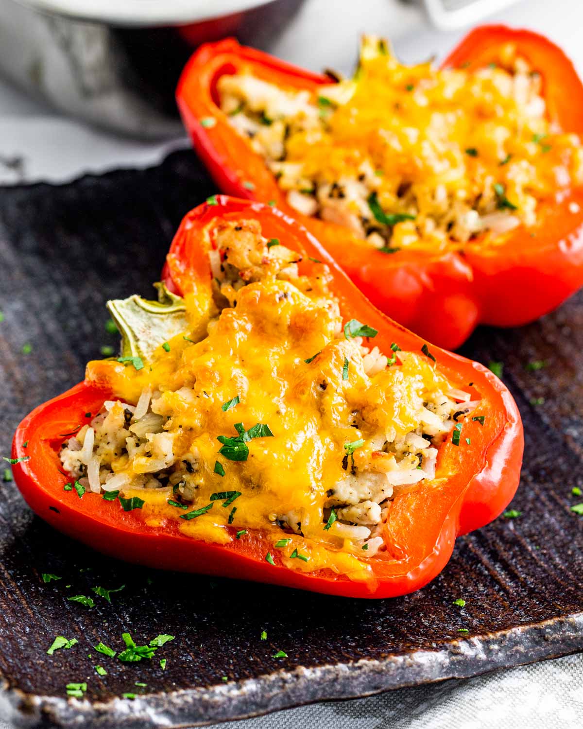 sideview shot of 2 stuffed pepper halves on a black plate topped with a bit of cheddar cheese and garnished with fresh parsley
