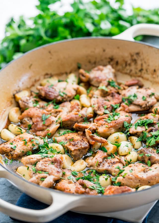 a braiser with chicken thighs, lots of garlic cloves, and parsley